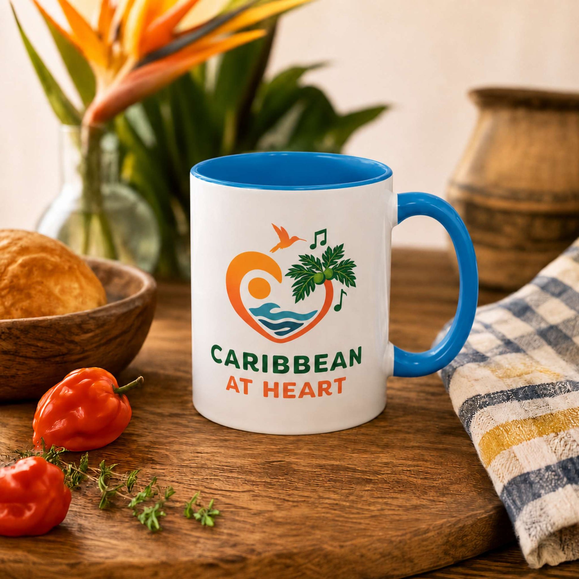 Caribbean At Heart logo accent mug with blue handle and interior featuring heart, hummingbird, waves and breadfruit leaves.