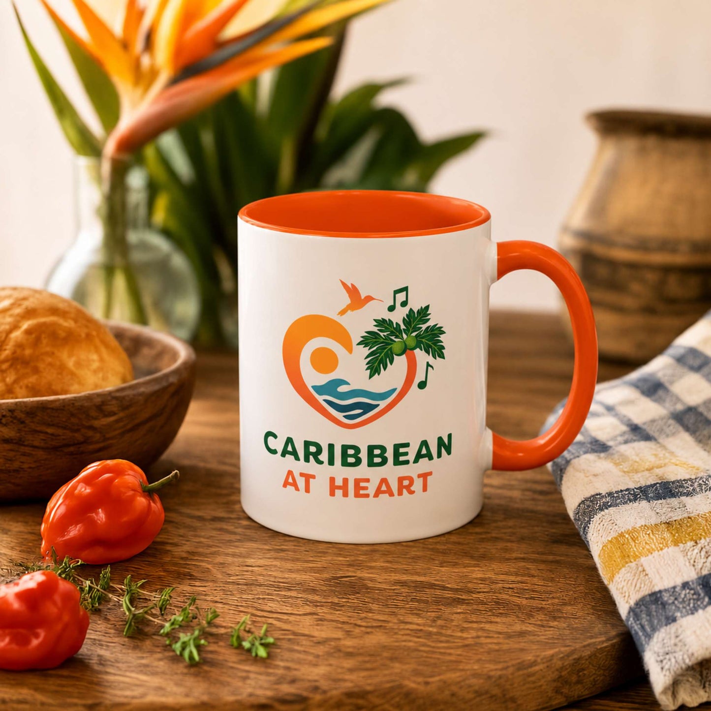 Caribbean At Heart logo accent mug with orange handle and interior featuring heart, hummingbird, waves and breadfruit leaves.