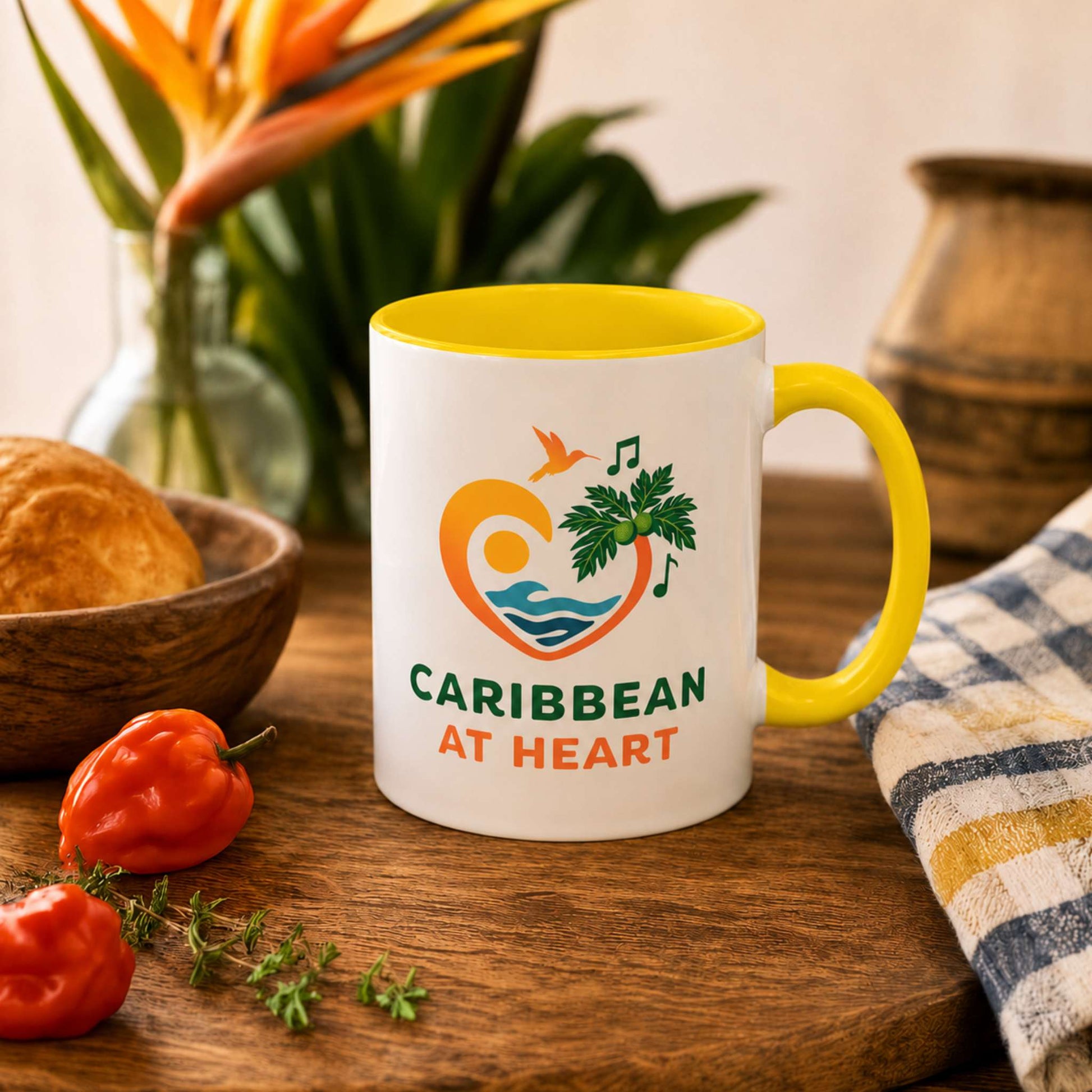 Caribbean At Heart logo accent mug with yellow handle and interior featuring heart, hummingbird, waves and breadfruit leaves.