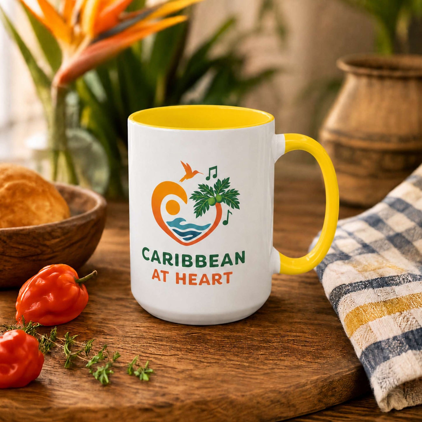 Caribbean At Heart logo accent mug with yellow handle and interior featuring heart, hummingbird, waves and breadfruit leaves.
