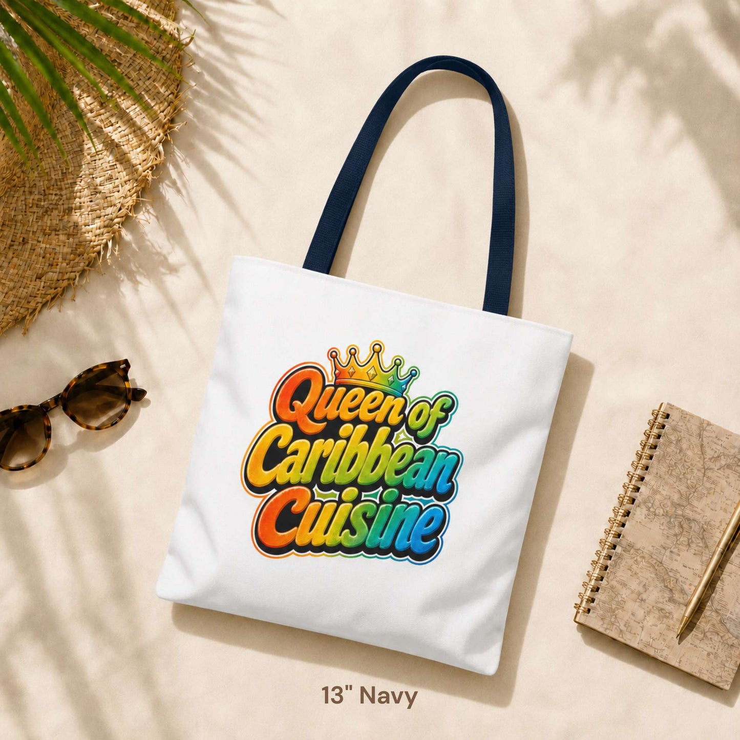 Queen of Caribbean Cuisine tote bag with colorful crown graphic and navy shoulder handles, available in three sizes.